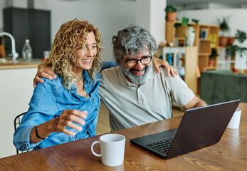 portrait of happy smiling senior elderly couple using a laptop computer and a credit card for online shopping at home, technology and internet use in everyday life concept