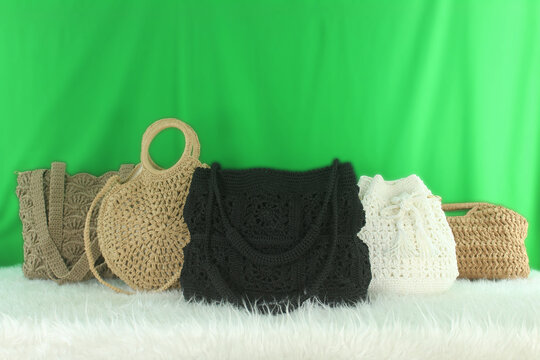 Crocheted bags in different colors and varieties arranged on a white fluffy blanket in front of a green background.