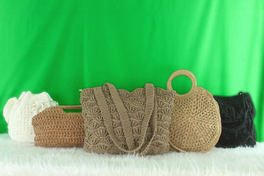 Crocheted bags in different colors and varieties arranged on a white fluffy blanket in front of a green background.