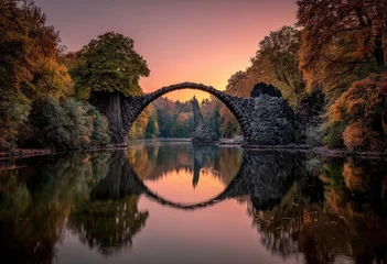Foto auf Acrylglas Rakotzbrücke Rakotzbrücke, also known as Devil's Bridge, perfectly reflected in the still water at sunset, surrounded by vibrant autumn foliage.  © mirna