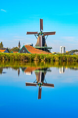 Symmetrical reflection of a windmill in water, with a background contrasting historic architecture (church) and a modern high-rise building