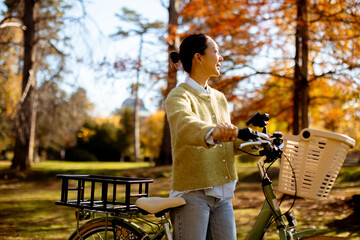 Joyful young woman enjoys autumn day in the park with a bicycle nearby