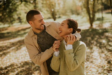 Fototapeta premium Happy couple enjoys a playful moment in a sunlit autumn park