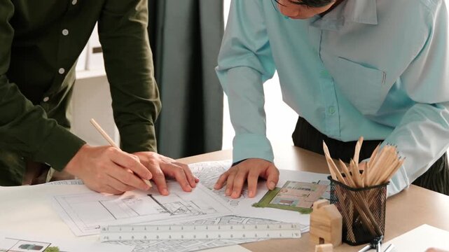 Smart architect and safety engineer discussion about building blueprint on table with architectural document, measurement tools and wooden block scatter around at modern office. Closeup. Delineation.