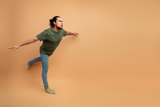 Young man in casual outfit leans against beige wall in energetic fashion lifestyle image