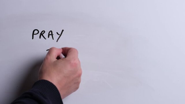 A person is writing Pray to Jesus in black marker pen on a whiteboard, perfect for Christian, religious themes, Church communications or faith presentations