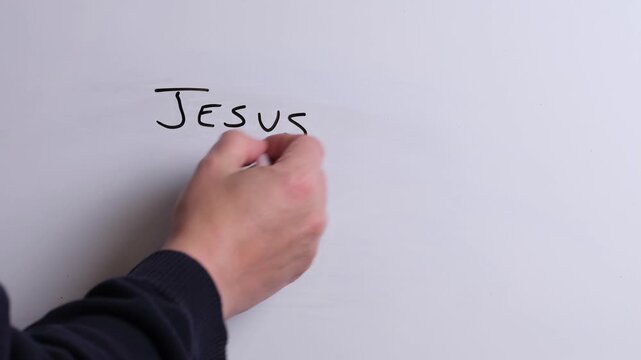 A person is writing Jesus is Risen in black marker pen on a whiteboard, perfect for Christian, religious themes, Church communications or faith presentations