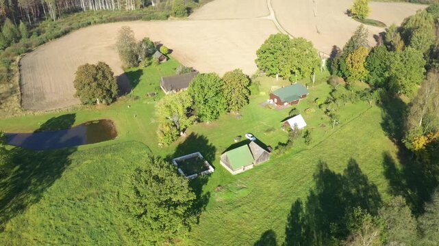 Aerial view of serene countryside landscape showcasing lush greenery, rustic buildings, and tranquil pond, with camera smoothly panning to capture scene evolution