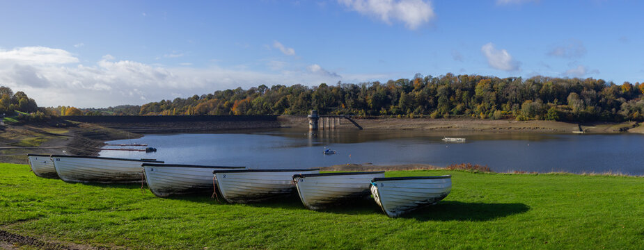Recreational boats moored on the grassy bank high above the dramatically low autumn water level exposed along the shoreline of Llandegfedd Reservoir near Pontypool, Torfaen, South Wales, UK