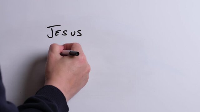 A person is writing Jesus Heals Hearts in black marker pen on a whiteboard, perfect for Christian, religious themes, Church communications or faith presentations