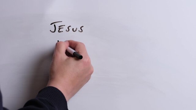 A person is writing Jesus Heals Hearts in black marker pen on a whiteboard, perfect for Christian, religious themes, Church communications or faith presentations