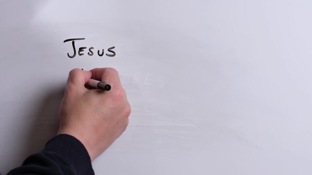 A person is writing Jesus Reigns Eternal in black marker pen on a whiteboard, perfect for Christian, religious themes, Church communications or faith presentations