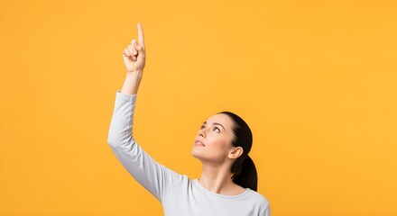 Young woman pointing upwards with curiosity against a vibrant orange background
