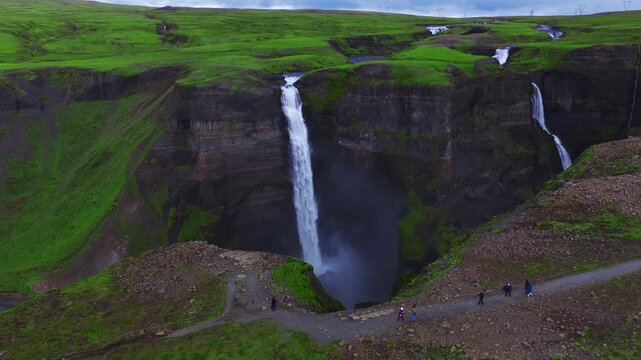 Aerial view shows Haifoss and Granni dropping into a basalt canyon in Thjorsardalur, Iceland. Overcast light, mist, braided river, and visitors on a cliff path. Stranger Things waterfall.