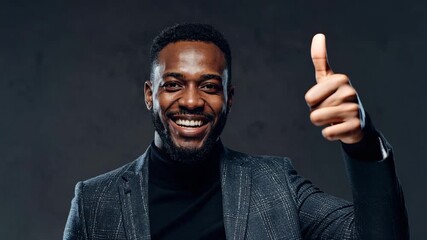 Portrait of a happy, smiling African American man in a stylish jacket and turtleneck, under a spotlight on a dark background.