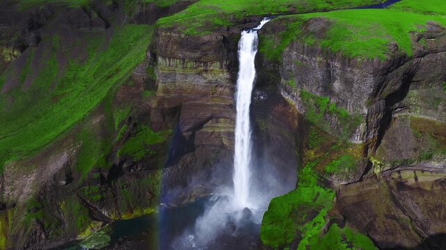 Aerial drone view shows Haifoss and Granni in Thjorsardalur, Iceland. Water plunges into a rocky canyon, spray forms a rainbow, basalt columns and strata are visible. Stranger Things waterfall.