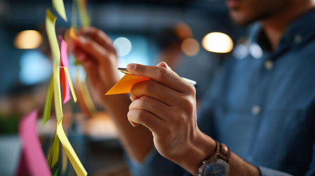 Faceless business people writing memos on colorful sticky notes defocused office meeting background planning strategy and brainstorming colleagues thinking concept creative pro