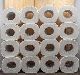 White toilet paper rolls arranged in geometric order on wooden table. Hygiene, sanitation, bathroom supply and cleanliness concept, minimalist product composition.
