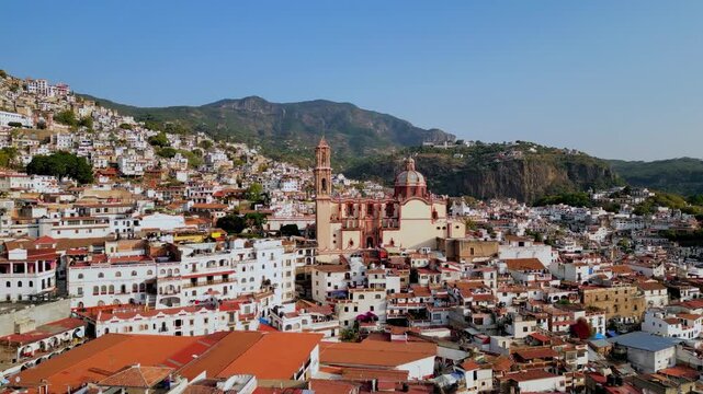 Aerial view flying toward Santa Prisca church with mountains and white houses in Taxco, Mexico