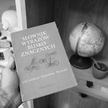 Vintage Polish dictionary of synonyms held in hand with globe and shelf in background