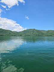 Serene Santa Maria del Oro Lagoon, Nayarit, Mexico. Calm green water reflects the blue sky and clouds. Lush hills create a tranquil natural landscape.