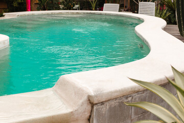 Beige concrete edges of the pool with clear water. Stylish curved pool for relaxation