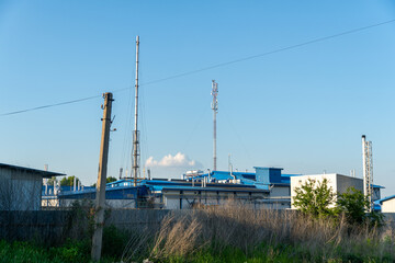 Communication towers and industrial buildings against a clear blue sky in a rural area during the day