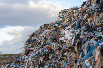 Waste pile rises at landfill site under cloudy sky in early afternoon light
