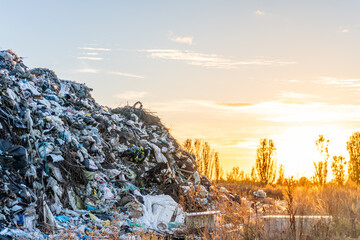 Large pile of trash under sunset sky at landfill site near trees in the background
