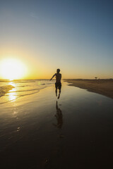 Naklejka premium Silhouette of sporty woman running and having fun on the beach during beautiful golden sunset over the sea. Active lifestyle by traveling, chasing sunrise und sunsets, freedom concept