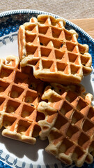 Delicious golden waffles on blue patterned plate in sunlight - perfect for cafes, breakfast restaurants, food bloggers concept of