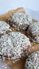 Raw breaded burger patties on paper: fresh ground meat with breadcrumb coating - concept for grocery stores, food blogs, cooking channels
