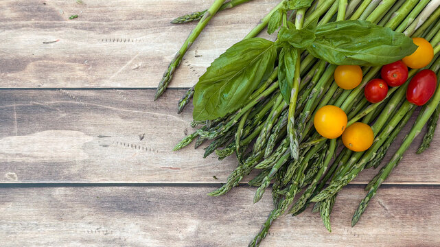 Fresh asparagus and cherry tomatoes with basil on rustic wooden table - concept of farm-to-table, culinary arts, organic produce