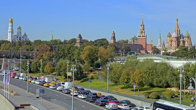 Russia, Moscow - October 01, 2025: Scenic view of the Moscow Kremlin, Cathedral of the Annunciation, and Saint Basil Cathedral along the Moskva River with cars driving on the embankment under clear bl