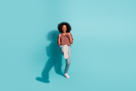 Young female model in casual print shirt jeans kicks with joy against blue background stock photo