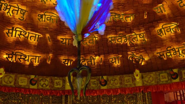 Colorful Trishul and balloon decoration against illuminated Hindi script temple wall