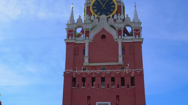 Spasskaya Tower clock on Moscow Kremlin with golden face and Roman numerals against red brick architecture. Famous Russian landmark timepiece showing historic ornate design under clear blue sky.