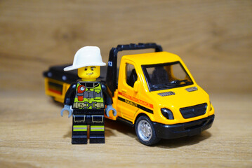 Obraz premium Lego firefighter figure stands next to a yellow toy truck on a wooden surface