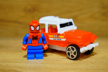 Obraz premium Spider-Man Lego figure stands next to a toy fire truck on a wooden surface