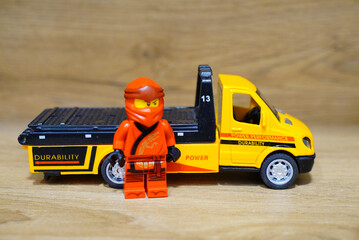 Obraz premium Lego Ninjago Jay minifigure stands next to a yellow toy truck on a wooden surface