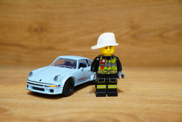 Obraz premium Lego Firefighter and Light Blue Porsche Toy Car on Wooden Surface