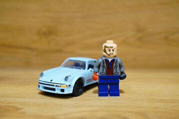 Fototapeta premium Lego figure with a toy Porsche car on a wooden surface
