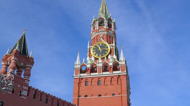 Spasskaya Tower clock on Moscow Kremlin with golden face and Roman numerals against red brick architecture. Famous Russian landmark timepiece showing historic ornate design under clear blue sky.