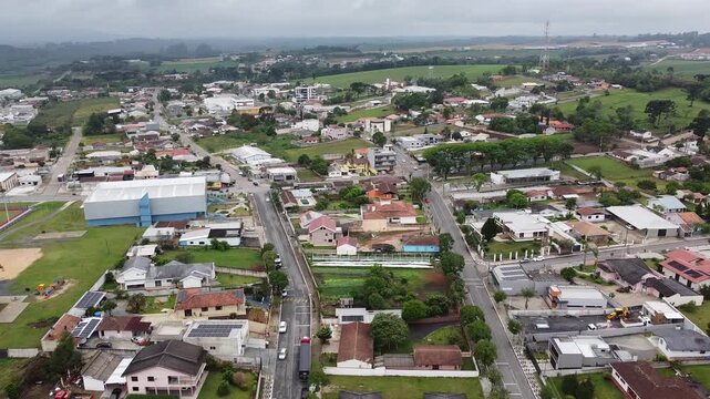 Aerial view of the city of Balsa Nova, near Curitiba, where a main street divides the landscape, with a church, a square, and several buildings on a slightly cloudy day.