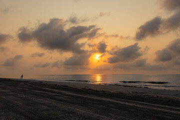 Sunrise on the beach with 2 fishermen in the background.