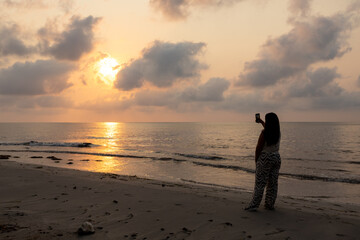 Woman on the beach taking pictures of the sunrise.