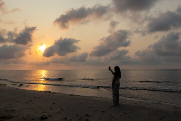 Woman on the beach taking pictures of the sunrise.