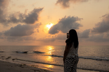 Woman on the beach taking pictures of the sunrise.