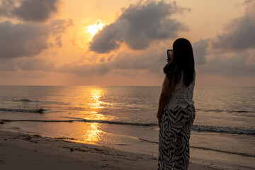 Woman on the beach taking pictures of the sunrise.