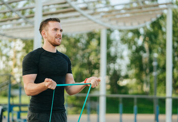 A man performs jumping jacks in an outdoor gym with urban towers in the background, filled with enthusiasm and athletic energy.